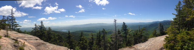 A panoramic view that captures rolling trees, misty hills, and mountains in the distance.