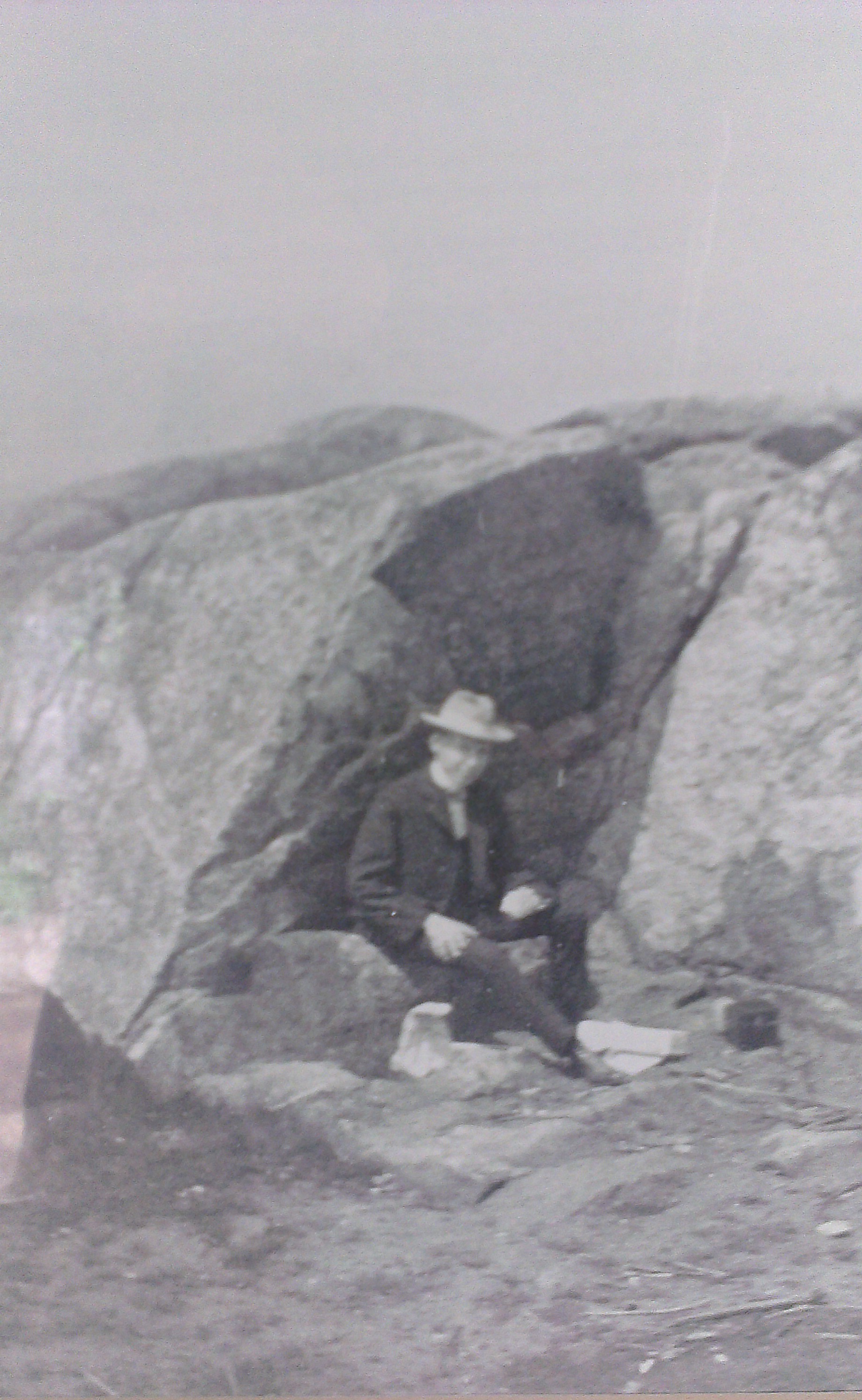 A hiker finds comfort in the "Cellar", many years before any buildings were constructed at Monadnock's Summit. This full photograph can be viewed in the Monadnock State Park Visitor Center.