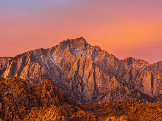 A mountain is lit orange and pink by sunset.