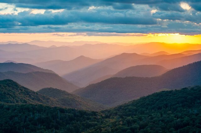 Several mountains and ridges form a landscape as the sun sets.